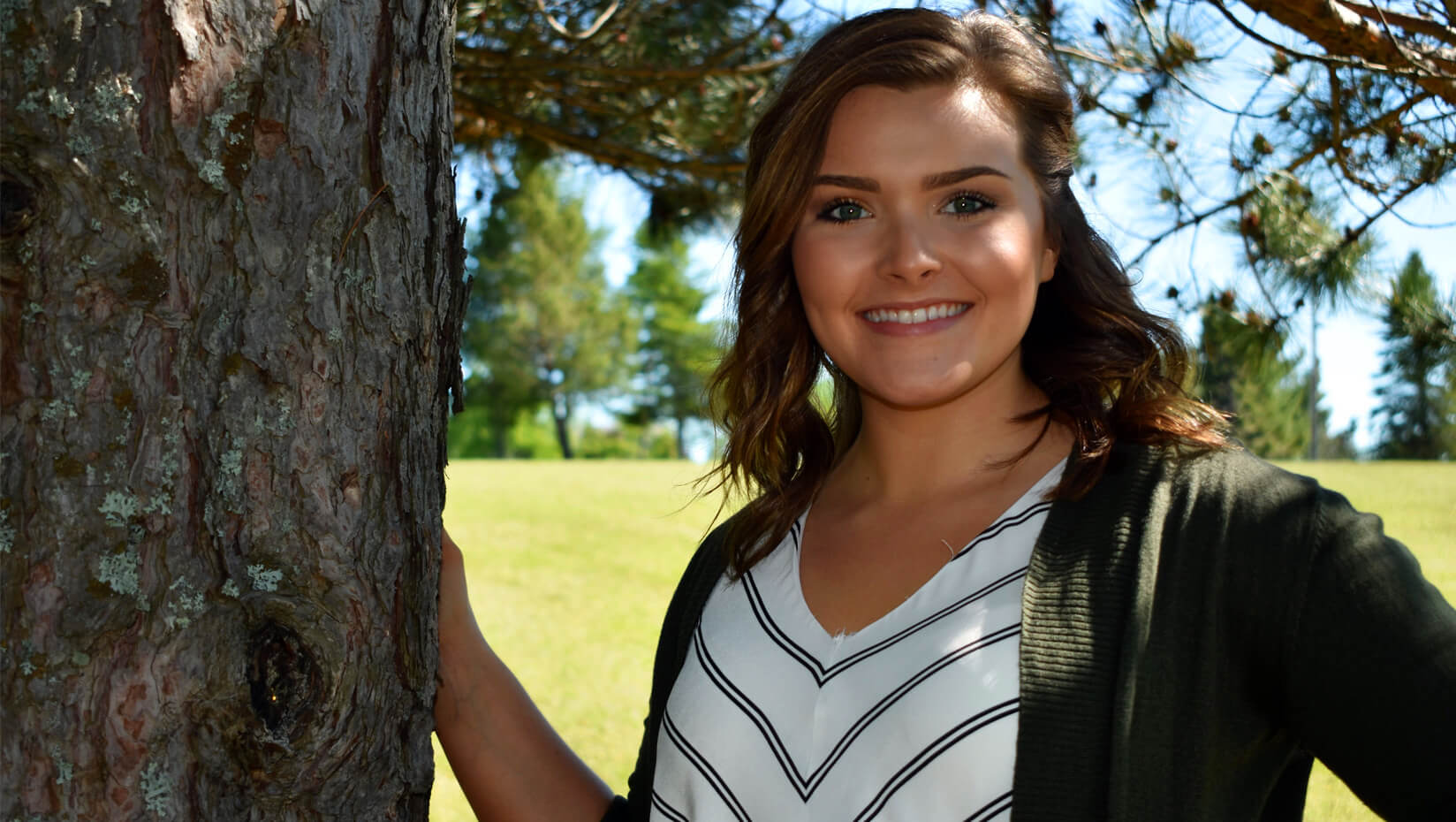 female student posing next to tree