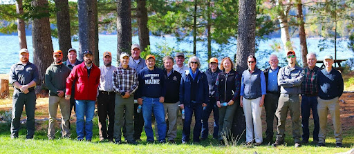 The people who attended the tour stand in a group in front of a tree trunks with a lake in the background. 