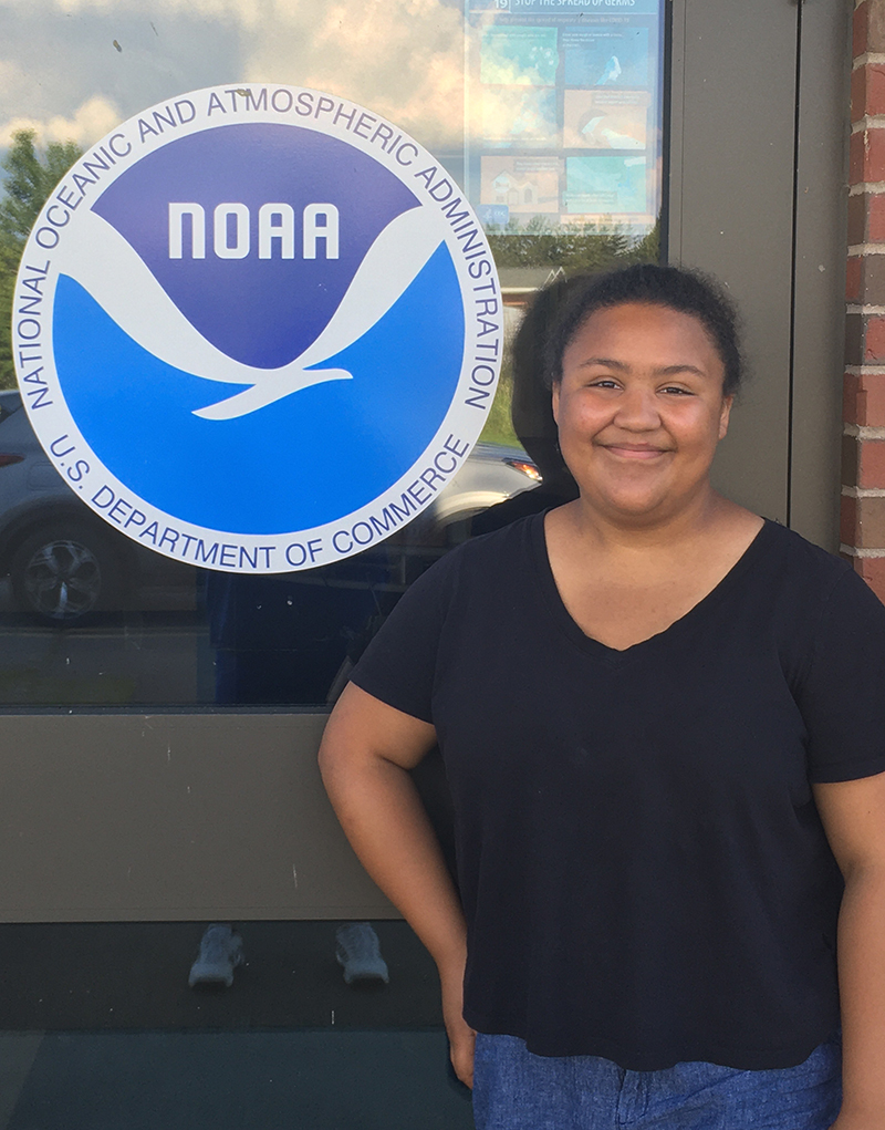 The author smiles at the camera while standing next to a sign for the National Oceanic and Atmospheric Administration