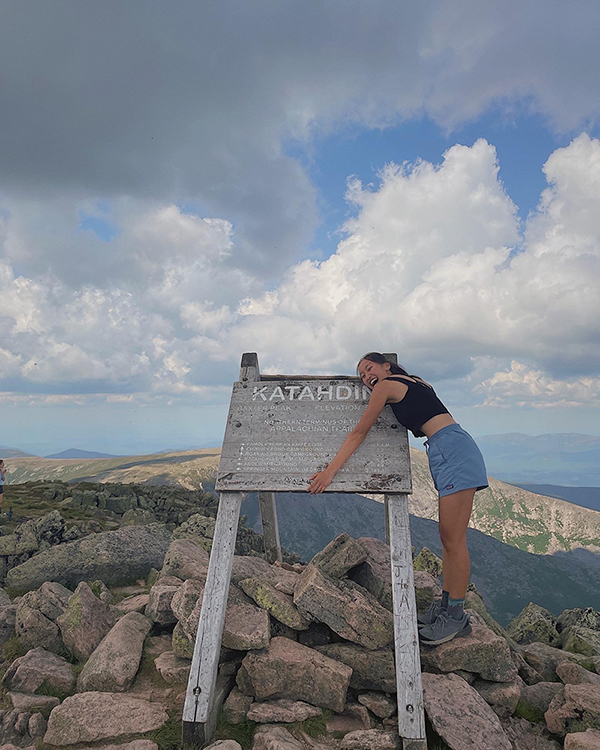 The author hugs a wood sign at the summit of Mount Katahdin.
