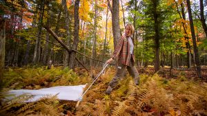 A woman conducts a tick survey in a forest by dragging a white cloth over the ground.